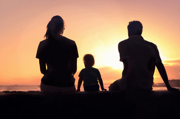 Silhouette of a young mum, son and dad watching the sunset