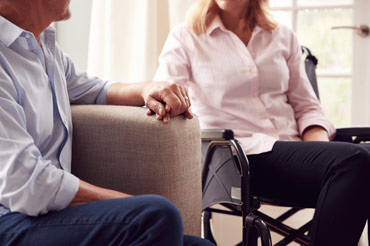 Wife sitting in a wheelchair holding her husbands hand